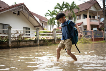 Asian boy struggles to walk across floodwater road with feet wearing sandals.