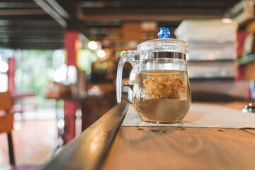 Glass teapot with herbal and flower tea brewing on a wooden table in a cozy cafe.