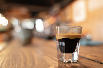 Close-up of an espresso shot on a wooden table with a blurred background.