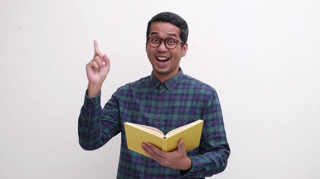 A man smiling happy and pointing up  while holding a book