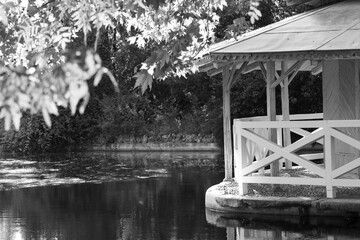 In a nostalgic corner, a wooden gazebo reflects in tranquil waters. Branches and light play with...