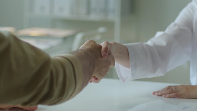 Handshake between unrecognizable female doctor and male patient sitting at table during medical consultation in clinic. Close-up shot