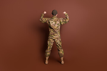 Full size photo of senior female courageous servicewoman show muscles back view wear camouflage uniform isolated on brown color background