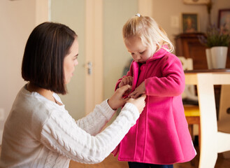 Mom, child and getting ready in home for kindergarten, play date and support in morning. Mother, girl and help in living room with coat, care and teaching with buttons for coordination development