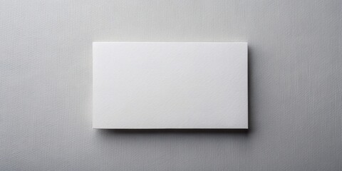 Empty white card positioned on a light grey table, seen from directly above, waiting for creative design or text to be added, isolated on a clean surface.