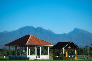 Two different size gazebos with a mountain in the background under the blue sky. Small buildings for farmers to take shelter and rest