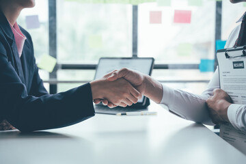 Sealing the Deal: Two professionals shake hands across a modern office desk, signifying a...