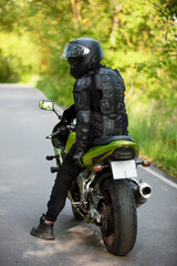 Fototapeta premium motorcyclist in black protective suit and helmet near green sports motorcycle