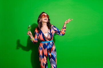 Photo of charming positive woman wear print overall enjoying champage celebrate xmas empty space isolated green color background