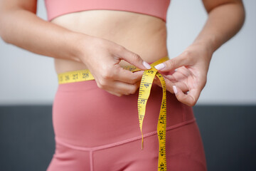 Woman is measuring her waist with a yellow measuring tape, checking the progress of her weight loss...