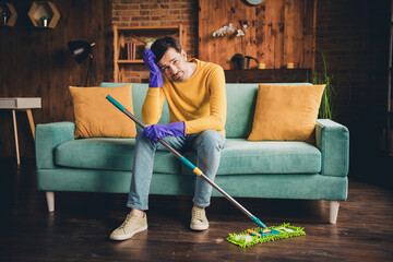 Full length photo of young guy mopping floor clean house sit couch tired dressed yellow garment...