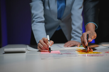 Business people working late in the office, using colorful sticky notes on a table to share ideas...