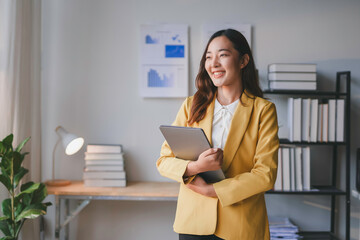 Young businesswoman is holding a laptop while looking out the window and smiling in her bright...
