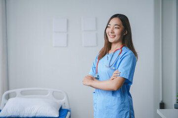 Young female doctor is smiling while standing in a hospital room with her arms folded
