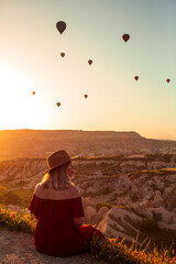 Beautiful girl sitting and looking to hot air balloons in Cappadocia, Turkey.