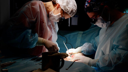 Man surgeon aided by team of professionals performs critical operation under bright lights of...