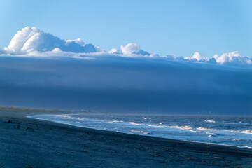 A tranquil beach stretches towards a dramatic sky, where a massive cloud formation dominates the horizon. Zhuangwei Township, Yilan County, Taiwan.