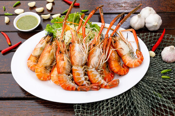 Lots of grilled river prawns are placed in woven containers and sauce bowls are decorated on a wooden background. seafood style