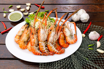 Lots of grilled river prawns are placed in woven containers and sauce bowls are decorated on a wooden background. seafood style