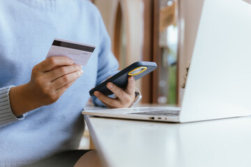 Woman at home making online payments on her laptop. She holds her credit card and enters the details on a secure e-commerce website, reflecting the convenience of online banking and shopping in the mo