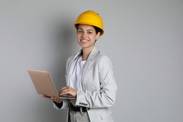 Engineer in hard hat with laptop on grey background, space for text