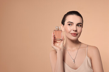 Beautiful woman with bottle of perfume on beige background. Space for text
