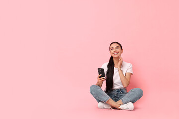 Smiling woman with smartphone on pink background. Space for text