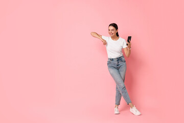 Smiling woman with smartphone on pink background. Space for text