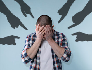 Silhouettes of people's hands pointing at upset man on light blue background. Social pressure,...