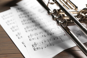 Trumpet and music sheet papers with notes on wooden table, closeup