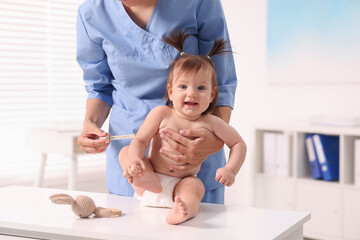 Pediatrician examining cute little girl with thermometer in clinic, closeup. Checking baby's health