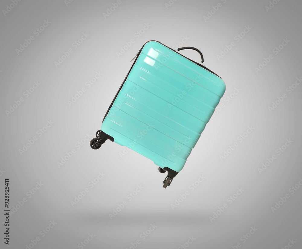 Wall mural Turquoise suitcase in air on light grey background