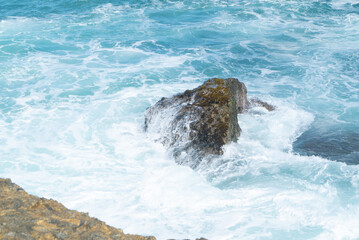 a large geologic formation of rock being pounded and splashed by strong current of sea water along a rocky coastal beach shore in the tropical region of the Pacific Ocean