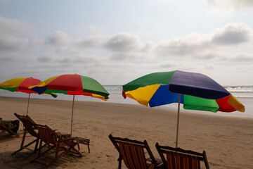 colorful umbrellas, each covering a pair of wooden chaise loungers facing the ocean and spread across the sand on a beachfront waiting for tourist to rent and sit for relaxation