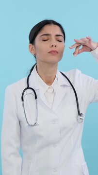 Irritated and annoyed Caucasian young adult doctor or nurse smelling disgust odor on blue background. Displeased and awful fragrance. Vertical video.