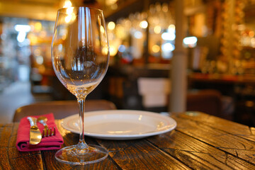 Elegant table setting in a cozy restaurant with empty wine glass, white plate, and silver cutlery on rustic wooden table