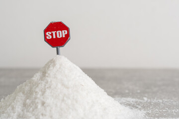 Red stop sign on pile of salt on gray background. Concept salt consumption.