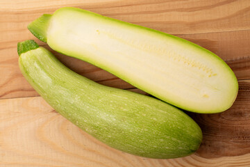 One whole and one half ripe zucchini on a wooden table, macro, top view.