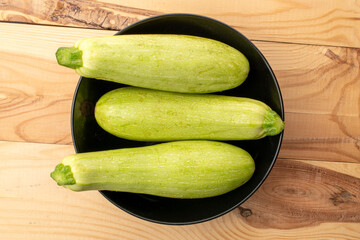Three ripe zucchini with a ceramic plate on a wooden table, macro, top view.