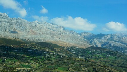 Fototapeta premium A stunning view of a rocky mountain range overlooking a lush green valley under a clear blue sky, highlighting the beauty of nature's contrast, Morocco. 
