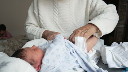 Grandmother changing newborn baby's diaper, gentle and nurturing care, intimate family moment,...