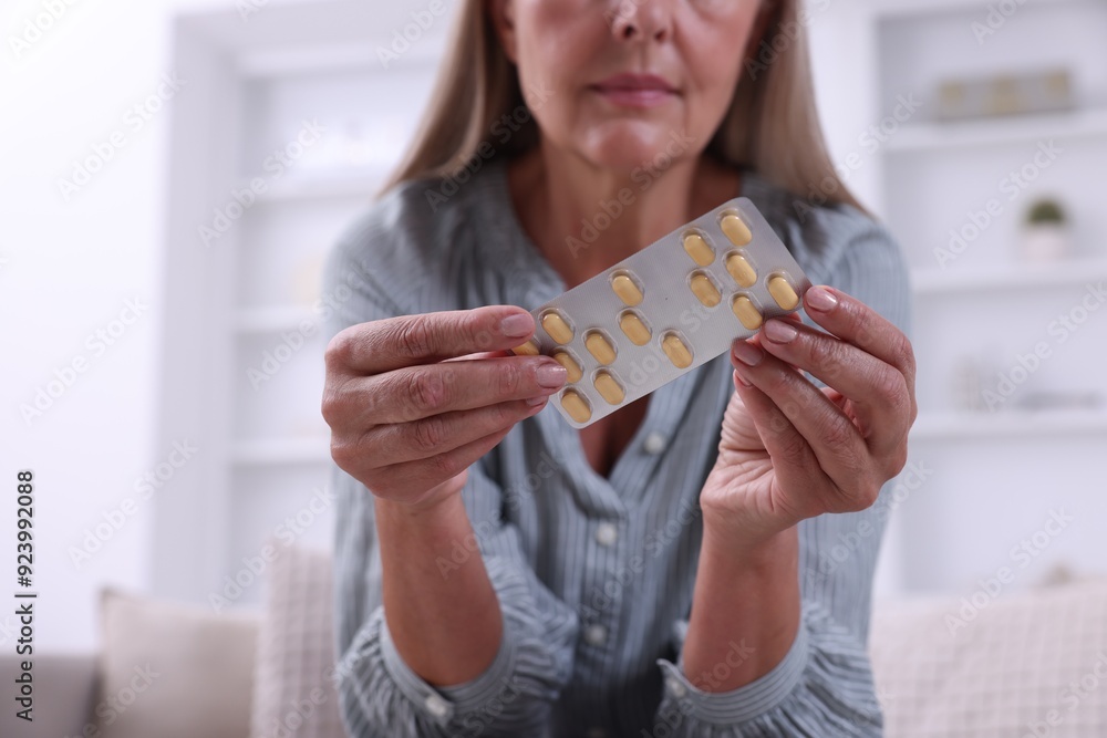 Poster Senior woman holding blister with pills at home, closeup