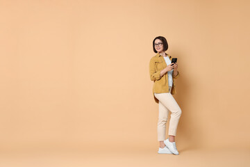 Smiling woman with smartphone on beige background. Space for text