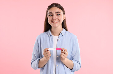 Happy woman holding pregnancy test on pink background