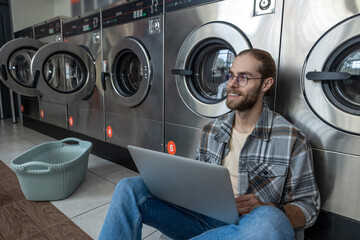 Man using technology for remote jo while waiting for laundry at self-service laundromat