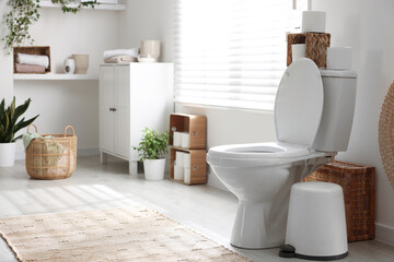 White toilet bowl, trash can and paper rolls in bathroom