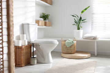 White toilet bowl, paper rolls and houseplants in bathroom