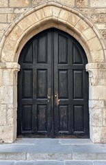 Black wooden double doors, with an arched top, set in an ancient stone wall