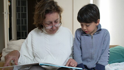 Grandmother pointing at a book page while reading to her grandson. educational aspect of storytelling and the close bond between generations through shared reading experiences