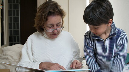 Grandmother pointing at a book page while reading to her grandson. educational aspect of storytelling and the close bond between generations through shared reading experiences